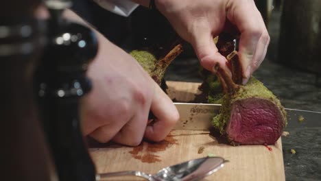 Chef-cuts-venison-meat-spiced-ribs-on-wooden-cut-board,-after-baking-in-oven