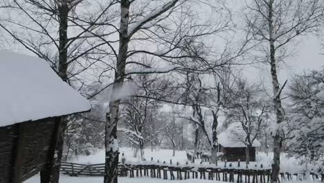 Drohne-Fliegt-An-Bäumen-Und-Schneebedeckten-Holzhütten-Vorbei,-Während-Es-Schneit