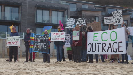 Demonstranten-Stehen-Zusammen-Am-Strand-Vor-Dem-Carbis-Bay-Hotel-In-St.-Ives,-Cornwall,-Mit-Schildern-Und-Plakaten-Zur-Demonstration