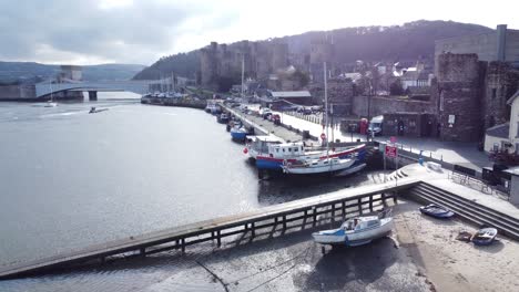 Idyllic-Conwy-castle-and-harbour-fishing-town-boats-on-coastal-waterfront-aerial-pull-back-low-descend