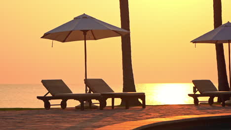A-dynamic-sunset-spills-yellow,-orange,-and-pink-on-sun-loungers-and-shade-umbrellas-poolside