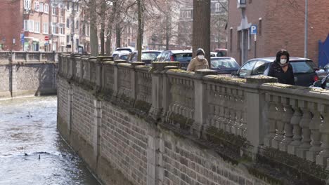 Masked-people-walking-next-to-river-Dijle-in-Leuven,-Belgium-during-coronavirus-pandemic
