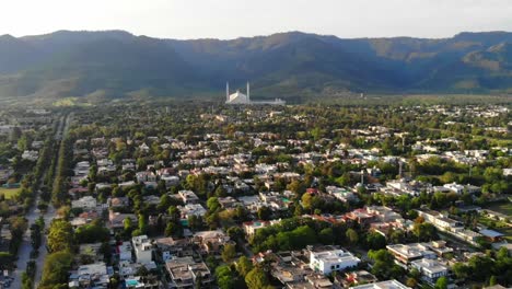 Vista-Aérea-Inclinada-Hacia-Arriba-Del-Paisaje-Urbano-De-Islamabad-Con-Faisal-Masjid-Revelada-Al-Pie-De-Las-Colinas-De-Margalla