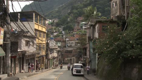 Tráfico-Vehicular-Y-Peatonal-A-Lo-Largo-De-Una-Calle-Angosta-En-Una-Favela-Construida-En-Una-Ladera-En-Río-De-Janeiro