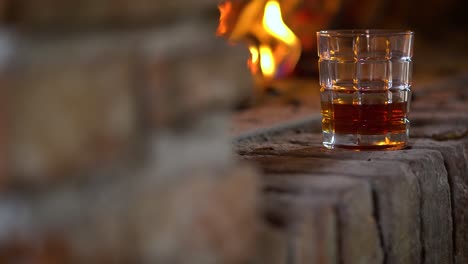 glass-with-a-drink-on-a-corner-of-a-chimneypiece-with-fire-burning-in-the-background,-static-shot