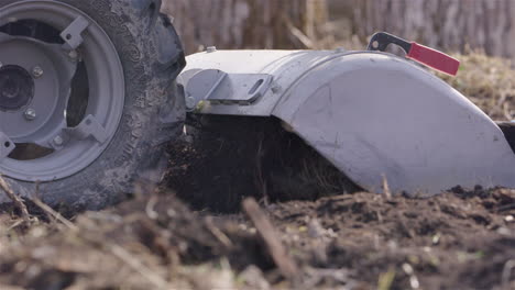 Rototiller-works-the-land,-agriculture-in-Sweden,-slow-motion-close-up-pan-left