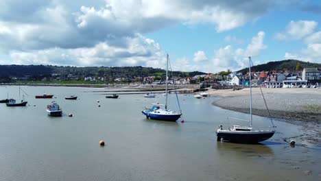 Aerial-view-moored-boats-on-Welsh-low-tide-seaside-breakwater-harbour-coastline-low-slow-left-orbiting-shot