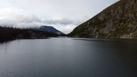 Drone-footage-of-Colchuck-Lake-near-The-Enchantments-in-Washington's-Cascade-Mountain-Range---Overcast-skies-and-low-lying-clouds-make-for-a-moody-shot---Fast-Flying-close-to-Lake-Water