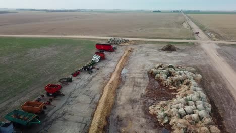 Aerial-view-of-a-line-up-of-agricultural-farm-equipment-and-large-grouping-of-partially-consumed-round-bales-of-hay