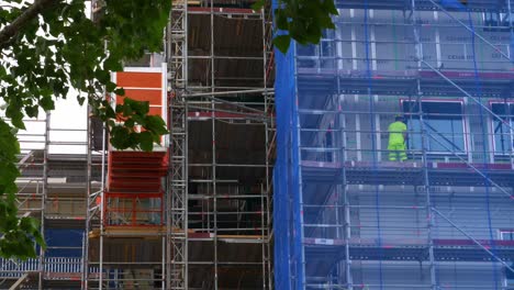 Construction-Site-Progress-with-Elevator-Going-Up-Side-of-Building-with-Workers-on-Site-Checking-Windows-in-Gothenburg,-Sweden