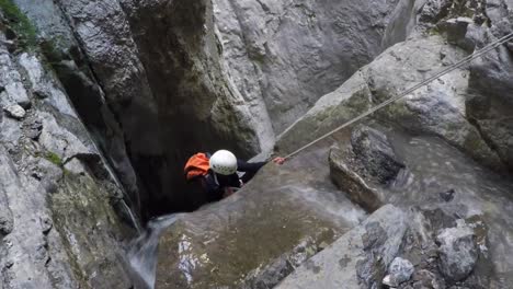 Woman-in-white-helmet-rappels-down-waterfall-into-river-canyon-below