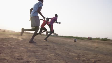 Varios-Chicos-Negros-Juegan-Un-Partido-De-Fútbol-Al-Aire-Libre-En-Una-Llanura-De-Tierra