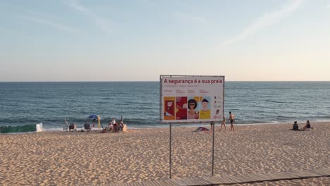People-walking-on-the-white-sands-of-Quarteira-Beach-past-safety-signs