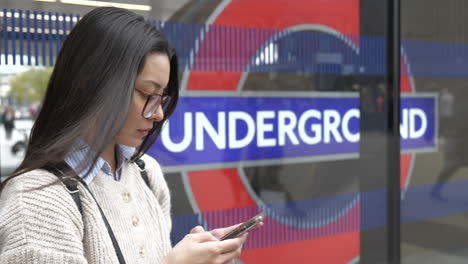 Attraktive-Junge-Asiatisch-amerikanische-Frau-An-Ihrem-Telefon-Außerhalb-Der-Londoner-U-Bahnstation