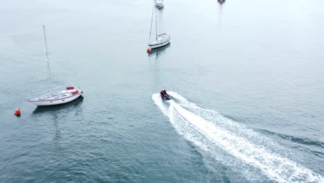 Jet-ski-navigating-river-Conwy-aerial-view-cruising-between-moored-sailing-ships-leaving-wake-in-sea