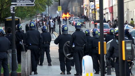Riot-police-stand-watching-people-gathered-around-a-burning-car-during-rioting-in-Hackney-following-the-fatal-shooting-of-Mark-Duggan-by-police