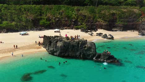 Aerial-view-of-Locals-jumping-off-of-a-boulder-at-Waimea-Bay,-Oahu,-Hawaii
