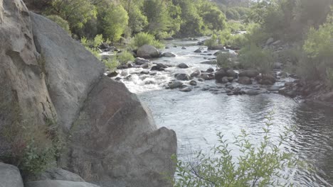 A-drone-flies-out-from-behind-a-set-of-rocks-revealing-a-tranquil-stream-and-river