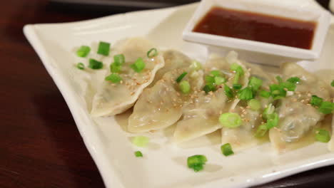 Restaurant-gyoza-pan-fried-steamed-dumpling-pot-stickers-plated-with-soy-dipping-sauce,-slider-close-up-4K