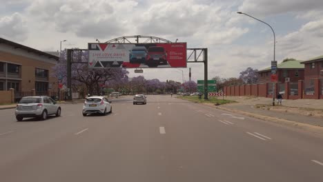 Jacaranda-trees-on-the-side-of-the-street-in-Pretoria-city,-POV-driving-shot