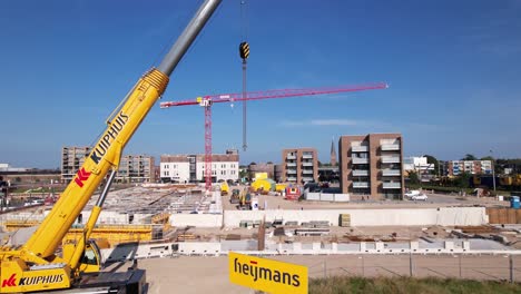 Backwards-aerial-movement-showing-sign-with-company-name-revealing-wider-construction-site-of-luxury-apartment-Kade-Zuid-complex-being-build-in-former-industrial-area-with-large-red-crane-in-the-back