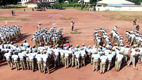 Jóvenes-Del-Servicio-Civil-En-El-Campamento-De-Nysc-Marchan-En-Formación-En-Un-Desfile---Vista-Aérea-Ascendente-Inclinada-Hacia-Abajo