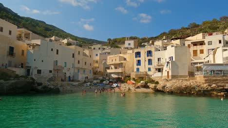 View-of-Levanzo-Sicilian-fishing-village-and-waterfront-scenic-bay-with-people-bathing-and-fishermen-boats-in-background-,-Sicily-in-Italy