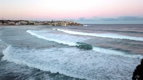 Schäumende-Wellen-Mit-Stadtbild-Im-Hintergrund-Während-Des-Sonnenuntergangs-Am-Bondi-Beach,-Sydney,-NSW,-Australien