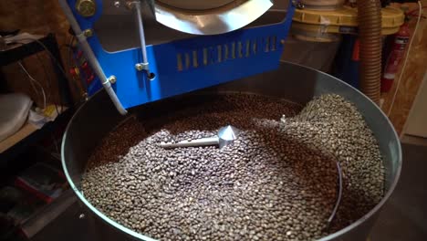 Professional-coffee-bean-roaster-mixing-and-turning-the-grains-with-steel-arms,-Handheld-shot