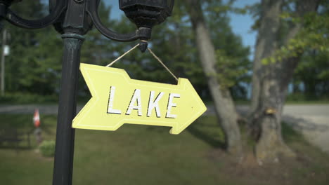 Pan-to-reveal-small-yellow-sign-pointing-to-the-lake-hanging-from-a-garden-lamp