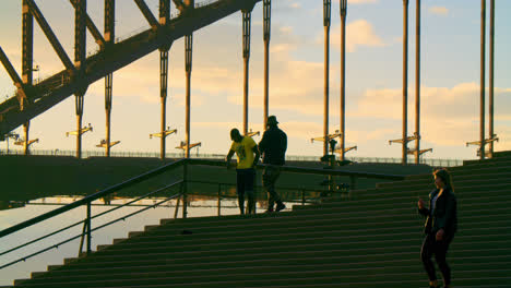 Silueta-De-Personas-Pasando-El-Rato-En-Las-Escaleras-Con-El-Puente-Del-Puerto-De-Sydney-En-El-Fondo-Al-Atardecer-En-Australia