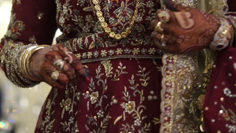 Manos-De-Novias-Asiáticas-Entrelazadas-Cubiertas-De-Un-Hermoso-Diseño-De-Henna-Con-Traje-De-Boda-Rojo