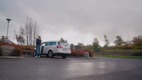 Junger-Großer-Mann-Mit-Mütze-Steigt-In-Sein-Weißes-Auto-Und-Fährt-Davon,-Statische-Totale