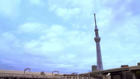 TOKYO-SKYTREE,-ASAKUSA,-TOKYO,-JAPAN-circa-April-2020:-trucks-and-cars-running-on-a-bridge-crosses-over-the-tracks,-train-runs-slowly