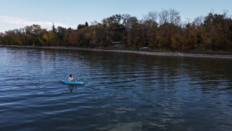 Woman-in-a-kayak-paddling-along-the-vibrant-shoreline-of-buffalo-lake-in-autumn