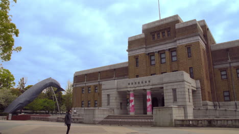 UENO,-NATIONAL-MUSEUM-OF-NATURE-AND-SCIENCE,-TOKYO,-JAPAN-circa-April-2020:-truck-passing,-man-with-mask-walking-by-in-front-of-NATIONAL-MUSEUM-OF-NATURE-AND-SCIENCE-on-quiet-cloudy-spring-day