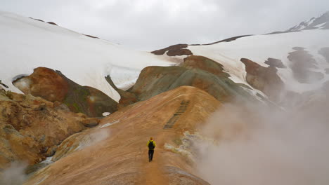 Aerial-wide-shot-of-man-with-backpack-walking-on-top-of-Kerlingarfjoll-Mountain-Range-in-Iceland---Smoke-is-rising-up-from-below