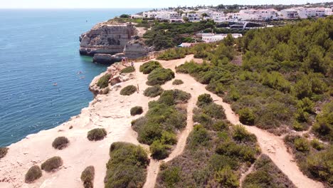 Cueva-De-Benagil,-Algarve,-Portugal---Vista-Aérea-De-Drones-Del-Pueblo-Y-La-Costa,-Entrando-En-La-Cueva-Con-Turistas,-Botes-Y-Kayaks