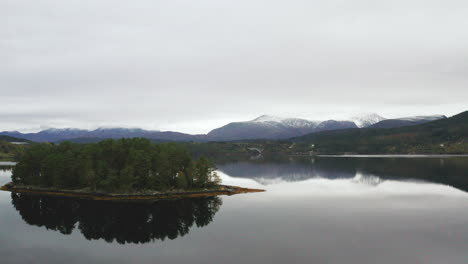 Spiegelreflexion-Auf-Einer-Ruhigen-Seelandschaft,-Umgeben-Von-Hügeln-Und-Schneebedeckten-Bergen-In-Norwegen