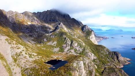 Panorama-Aéreo-Panorámico-En-Lo-Alto-De-Las-Montañas-Con-Un-Lago-De-Montaña-En-Las-Islas-Lofoten-En-El-Norte-De-Noruega-Con-Vistas-A-Las-Numerosas-Islas-Pequeñas-Repartidas-Por-El-Mar