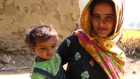 Joven-Madre-India-Con-Un-Niño-En-Brazos-Mirando-A-La-Cámara-Y-Sonriendo,-Pueblo-De-Noondpura-En-Rajasthan