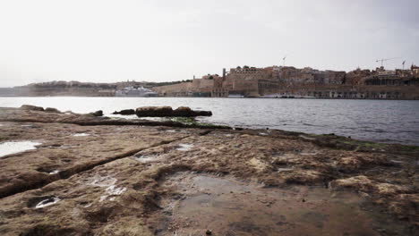 Dolly-forward-of-rocky-beach-with-Valletta-in-background,-Malta