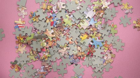Slow-Motion-Of-Puzzle-Pieces-Falling-On-Pink-Surface---overhead-view