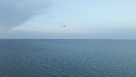 Wide-shot-of-red-Coast-Guard-helicopter-flying-over-calm-blue-ocean