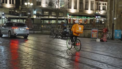 Cámara-Lenta-De-Un-Mensajero-De-Comida-Para-Llevar-Con-Ropa-Y-Casco-De-Seguridad-Que-Se-Dirige-A-Los-Clientes-En-Bicicleta-Por-La-Noche-En-El-Centro-De-La-Ciudad