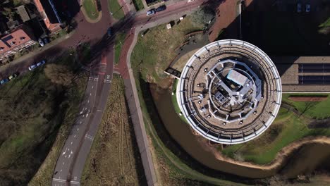 Cars-and-traffic-seen-from-top-down-aerial-view-slowly-revealing-round-towering-building-of-service-flat-elderly-residential-home-in-Dutch-tower-town
