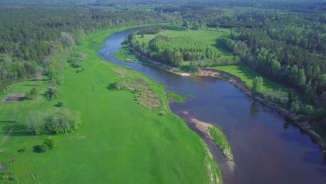 Aerial-birdseye-view-of-a-Venta-river-on-a-sunny-summer-day,-lush-green-trees-and-meadows,-beautiful-rural-landscape,-wide-angle-drone-shot-moving-backward