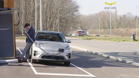 A-lone-man-on-his-mobile-device-leans-against-his-electric-car-at-a-public-charging-station