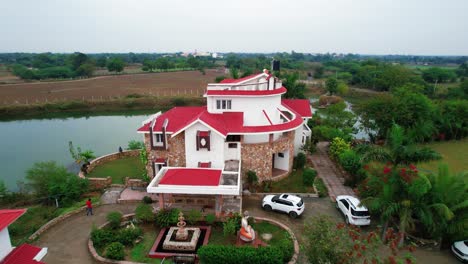 Drohnenaufnahme-Aus-Der-Luft,-Die-Von-Einem-Komplex-Schöner-Ferienhäuser-In-Vadodara,-Indien,-Zurückkehrt,-Umgeben-Von-Einem-Ruhigen-See-Und-Grüner-Vegetation-Für-Die-Zeit-Mit-Der-Familie