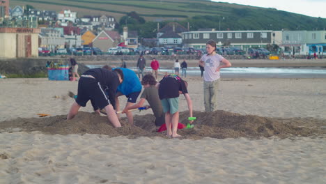 Grupo-De-Niños-Ingleses-Cavando-Arena-En-La-Playa-De-Perranporth-En-Cornwall,-Inglaterra---Tiro-Estático